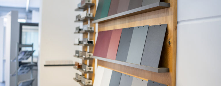 Auswahlwand im Showroom von Fensterbau Knipping mit Farbmustern und Profilschnitten für Fenster- und Türrahmen in verschiedenen Ausführungen.