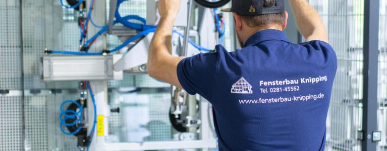 Mitarbeiter von Fensterbau Knipping bedient eine automatisierte Maschine zur Glasverarbeitung in der Produktionshalle.