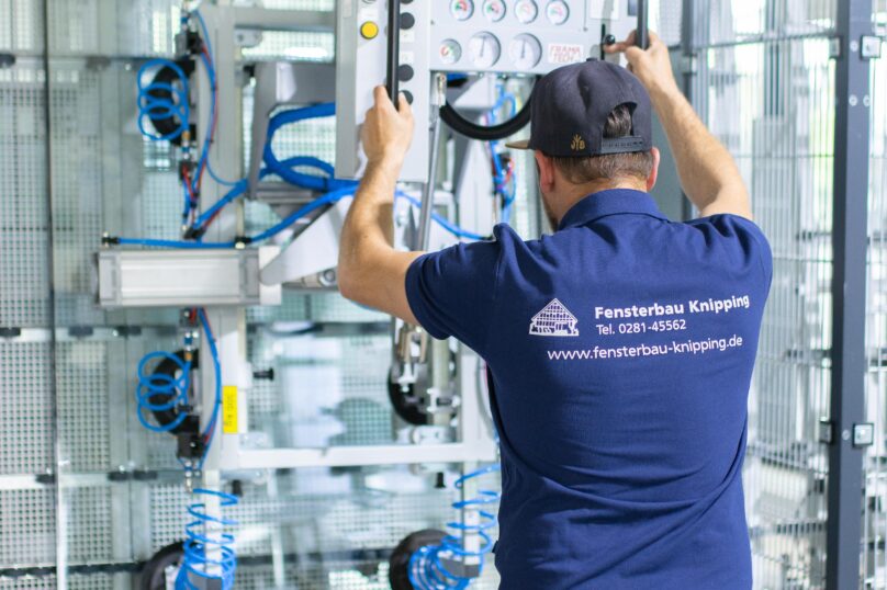 Mitarbeiter von Fensterbau Knipping bedient eine automatisierte Maschine zur Glasverarbeitung in der Produktionshalle.